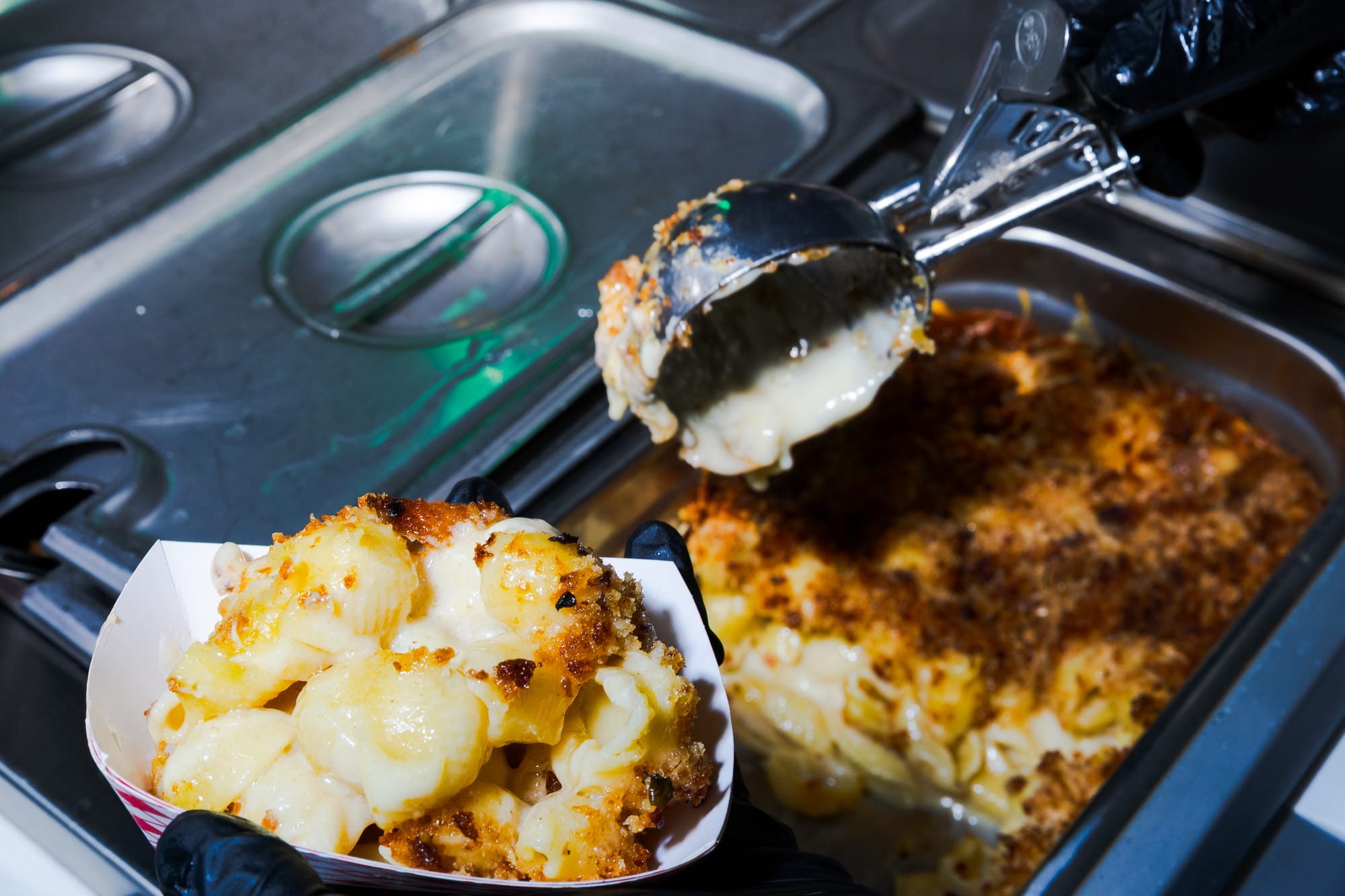 Macaroni and cheese being scooped into a paper bowl.