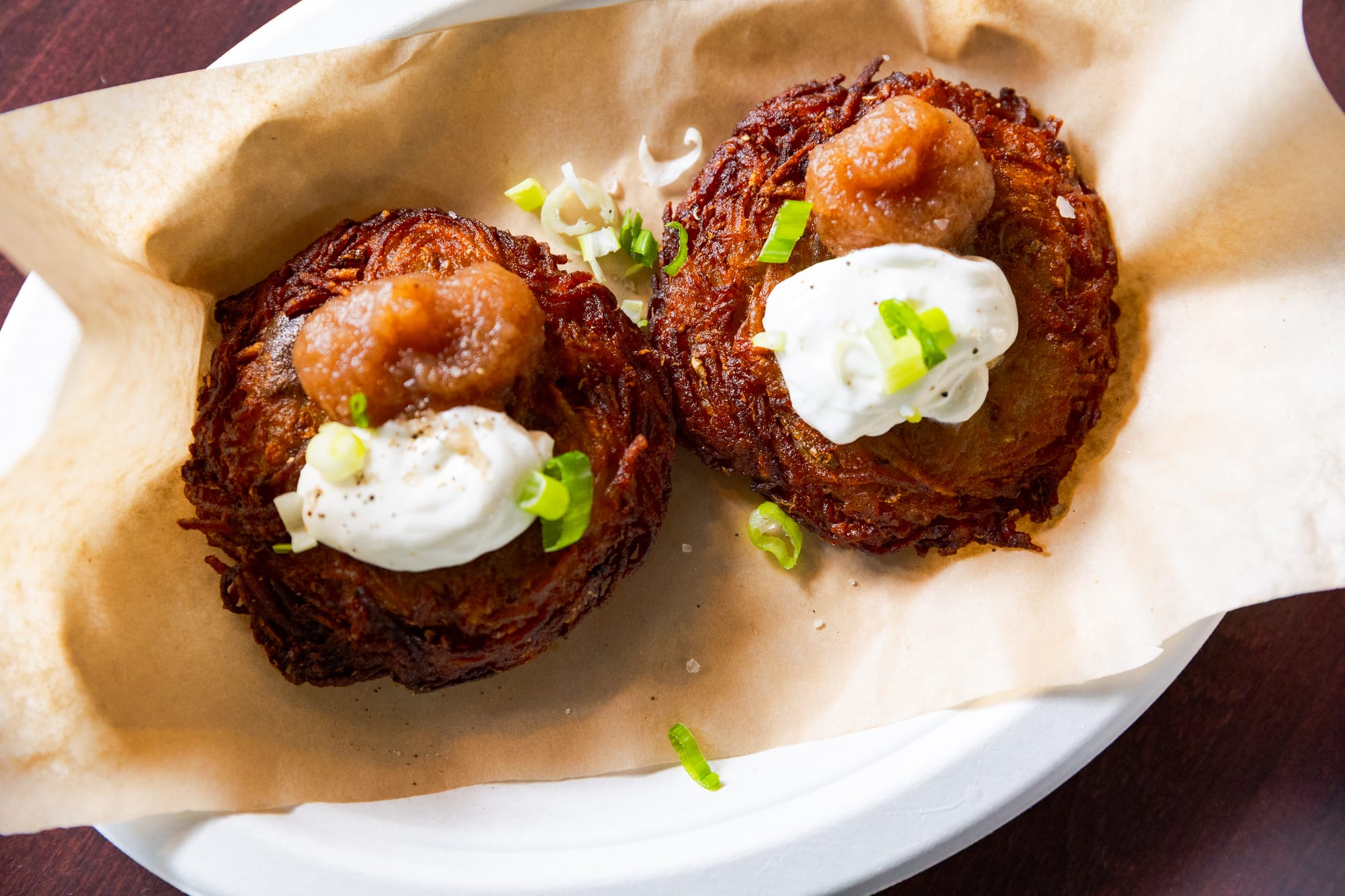 Two latkes on a plate with sour cream and applesauce.