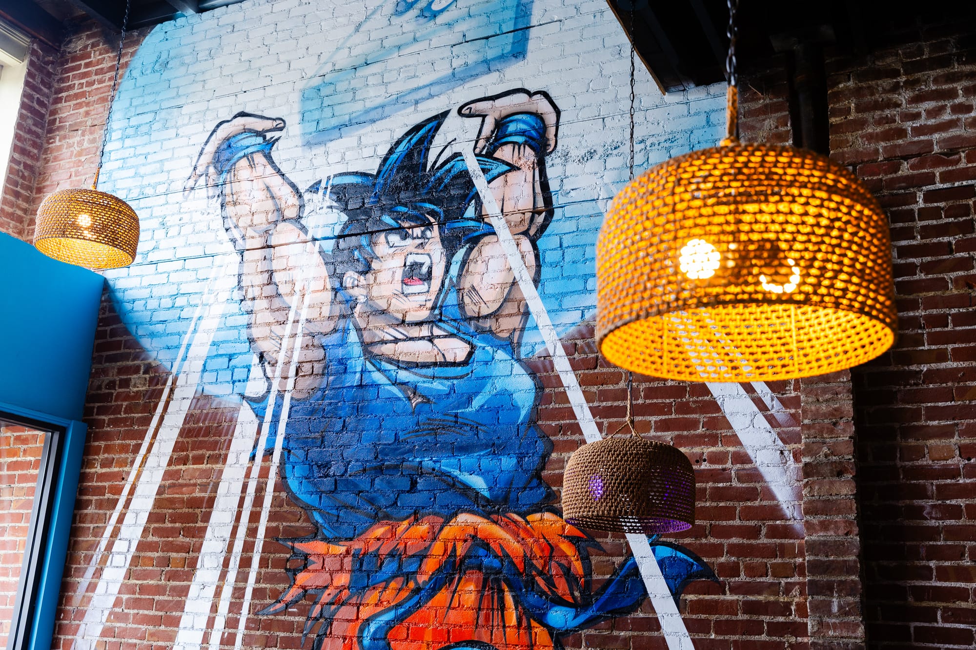 Painted mural of a spiky-haired anime character (Goku) raising his arms on a brick wall.