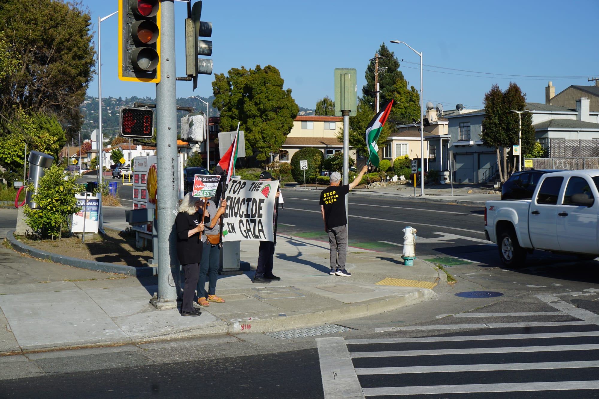 people stand in front of a gas station waving signs that read 'stop the genocide in gaza'