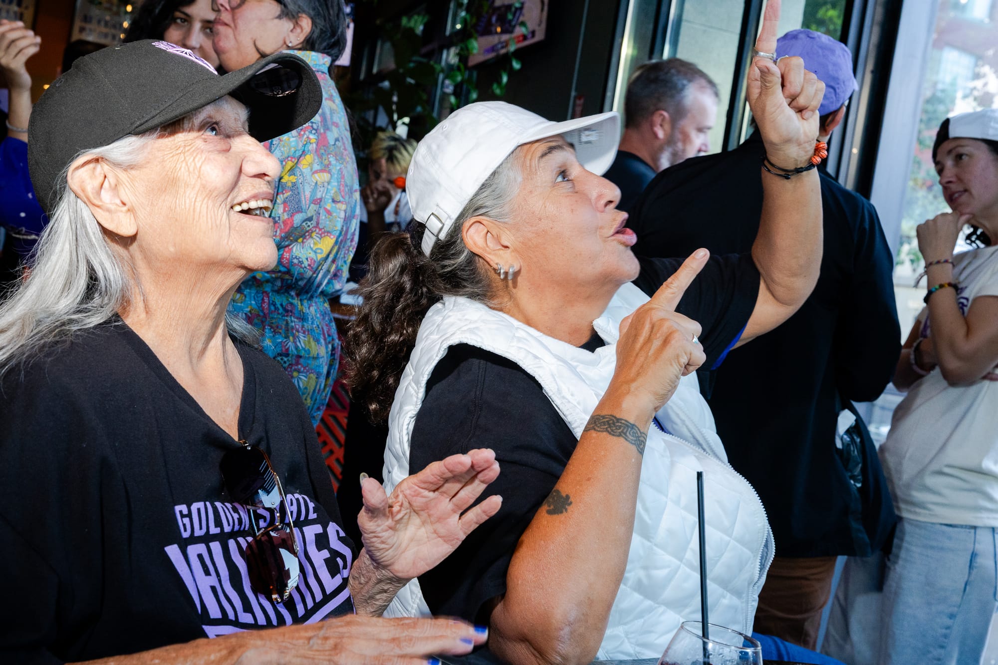 two older women smile while looking up and pointing in a sports bar
