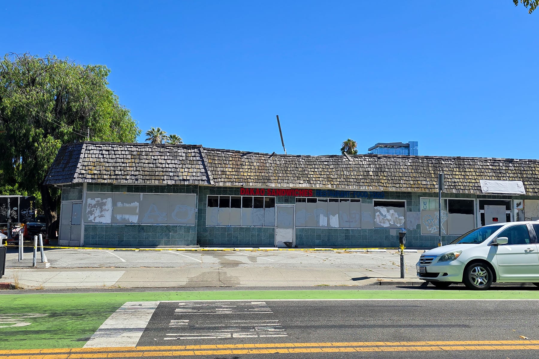A low and long building with a shingled roof and a sign that says "Dakao Sandwiches."