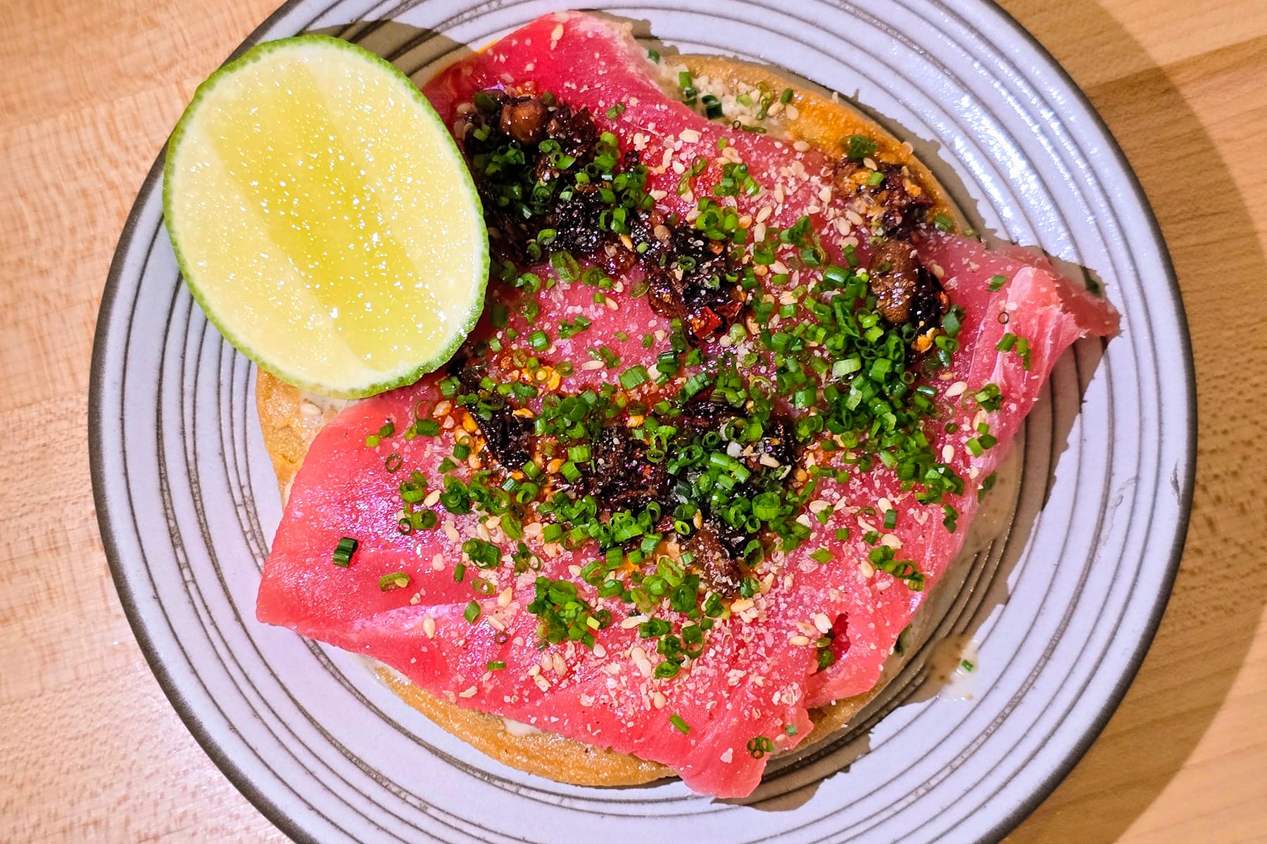 Tostada with a slab of red tuna meat on a spiral plate with a slice of lime.