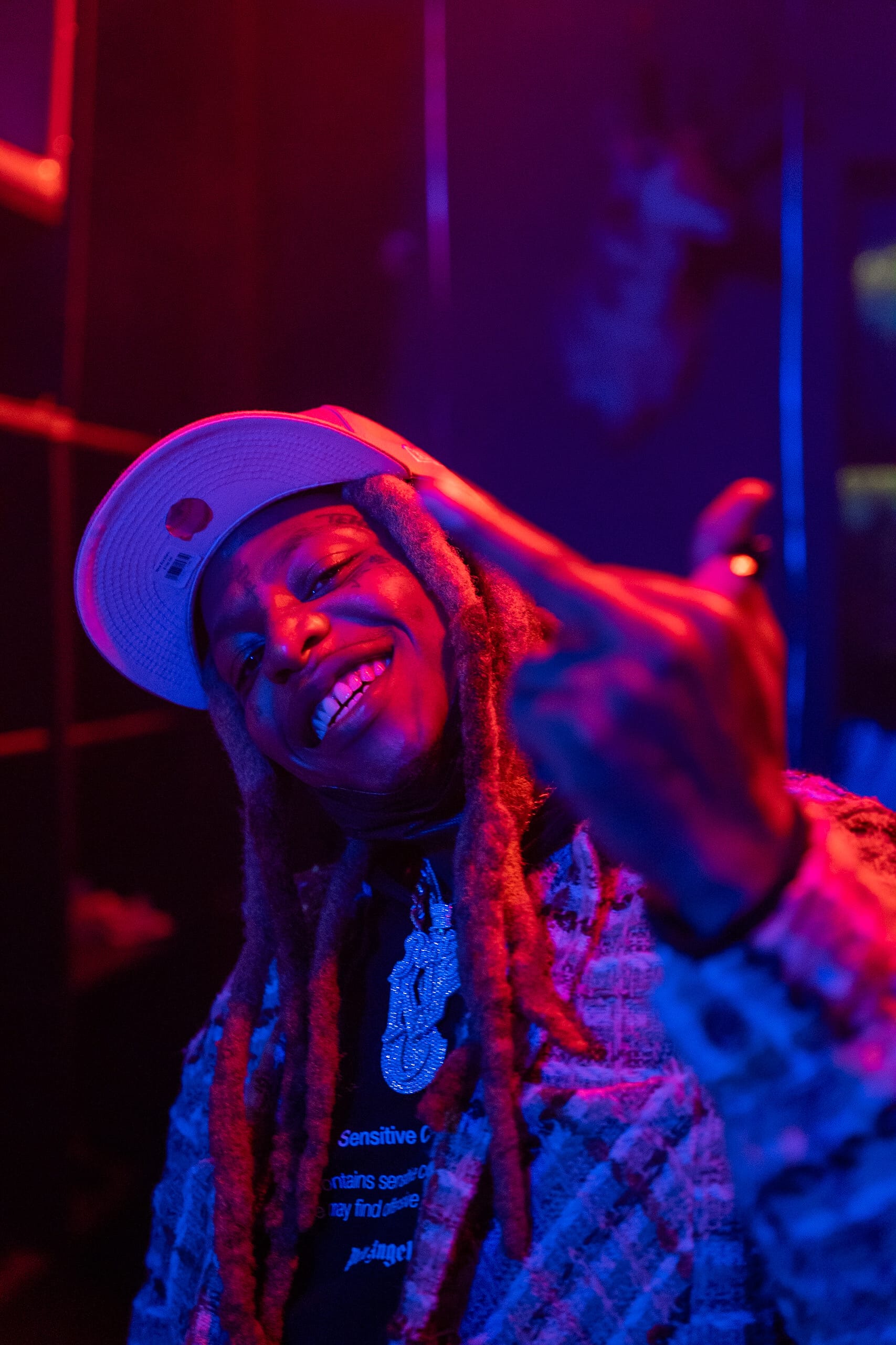 A man with dreadlocks points the middle finger of his left hand up while grinning.