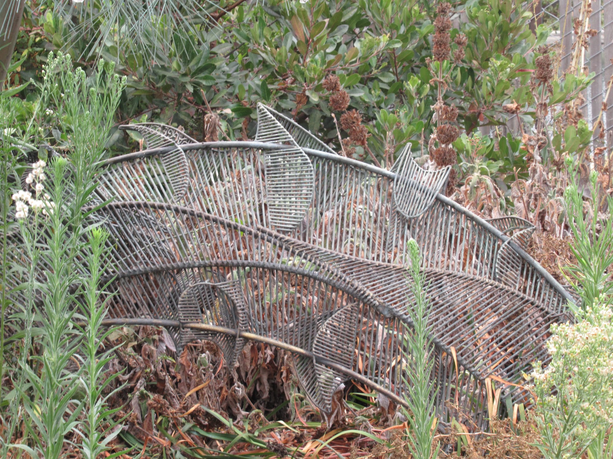 A closeup of the metal leaf that was at the bottom of the dandelion puffs. It is now surrounded by grass and weeds.