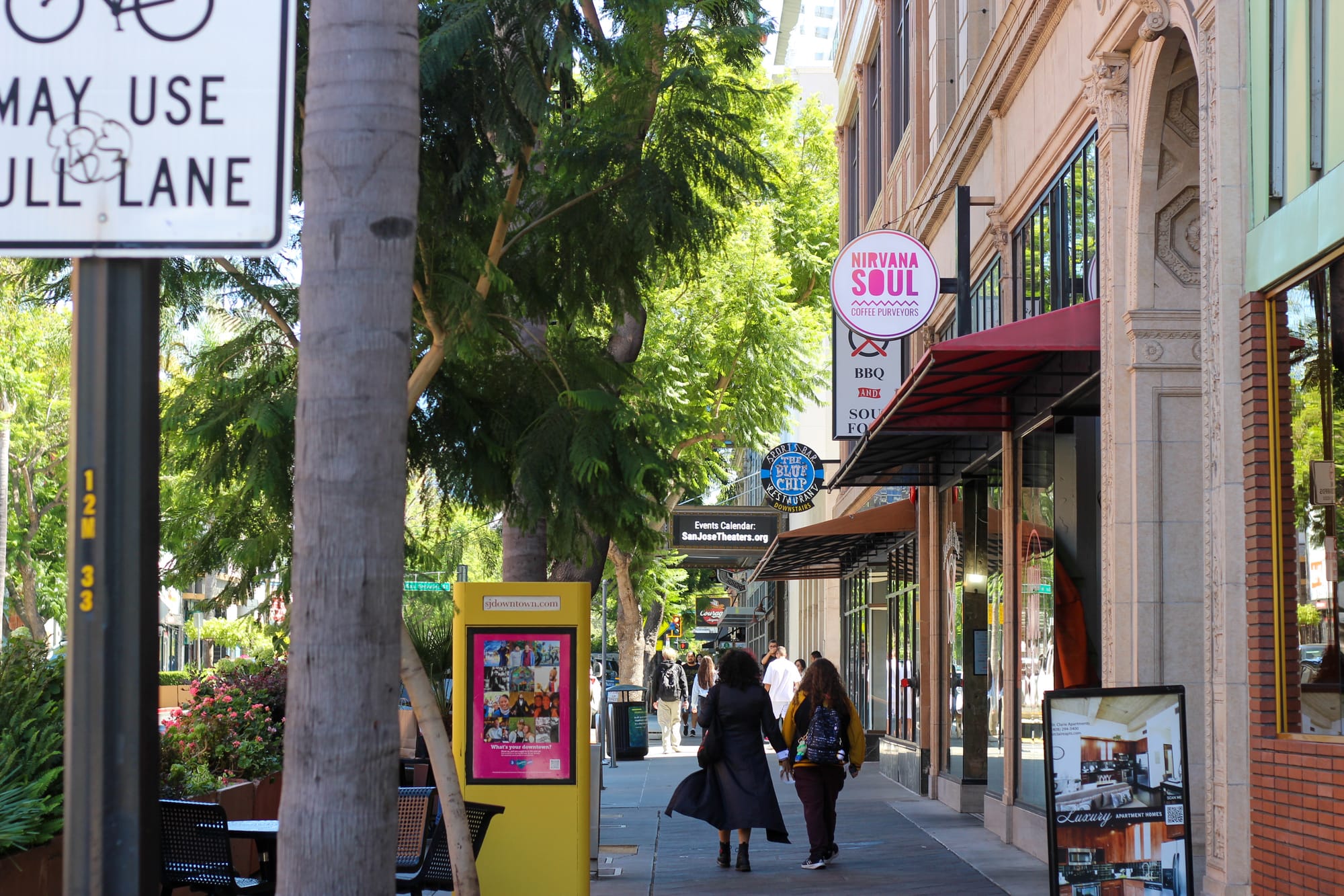 Two people walk along a sidewalk in front of storefronts: "Nirvana Soul," a "BBQ" spot, and Starbucks.