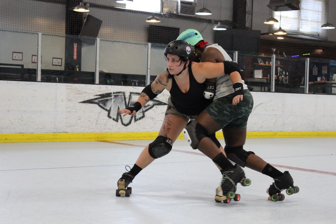 two skaters practicing blocking moves on the track, the one in the front is trying to keep the one in the back away
