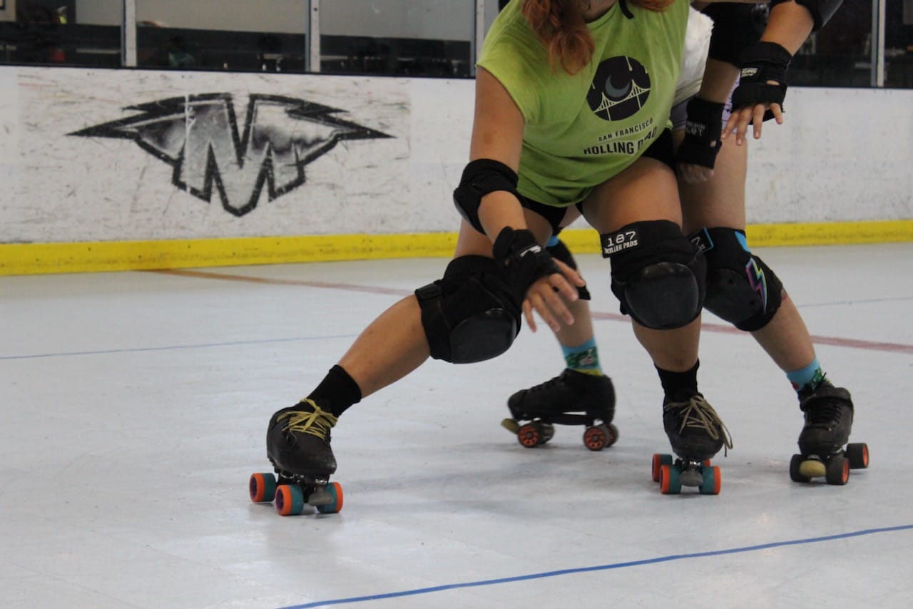 two skaters practicing blocking moves on the track, the one in the front is trying to keep the one in the back away
