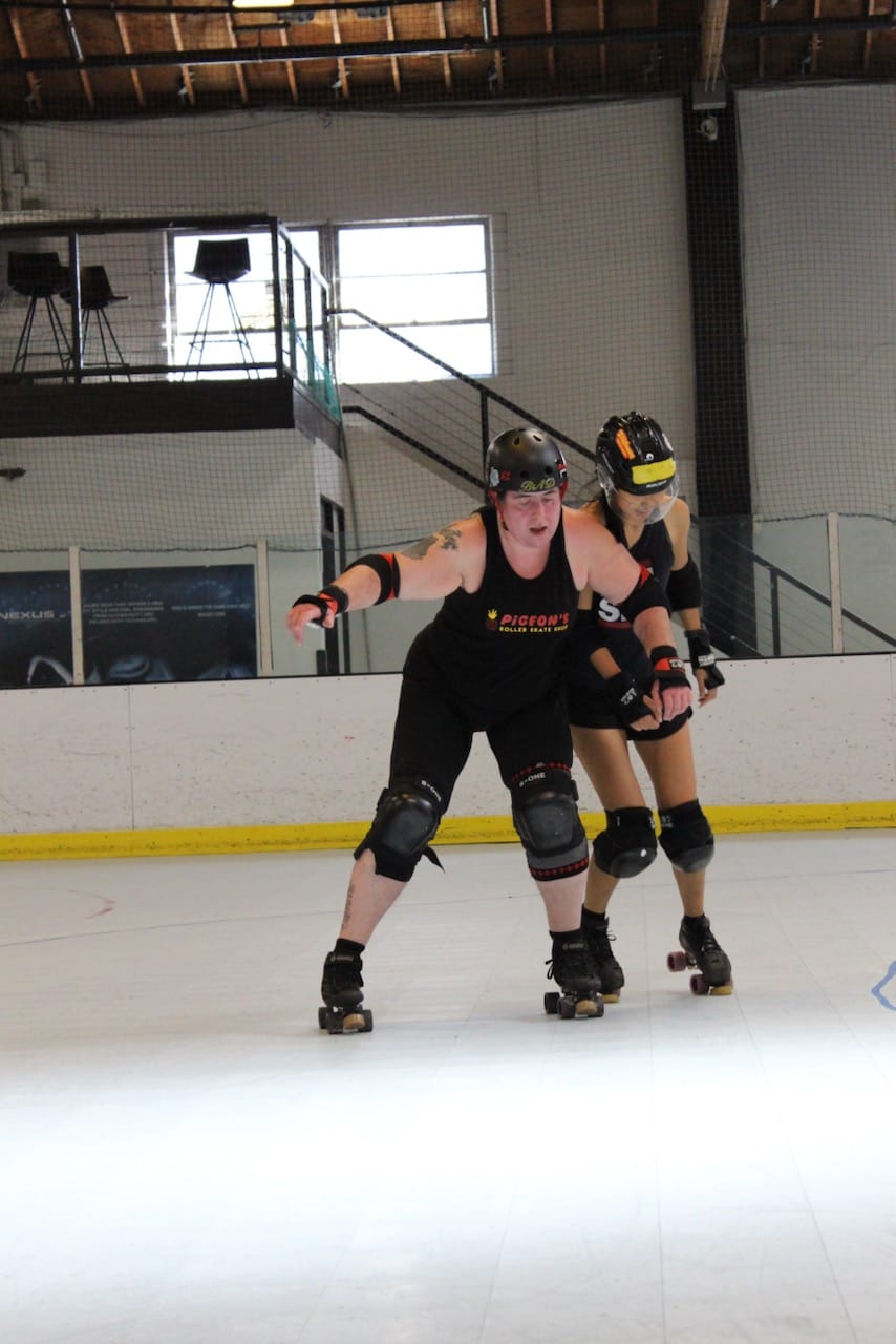 two skaters practicing blocking moves on the track, the one in the front is trying to keep the one in the back away