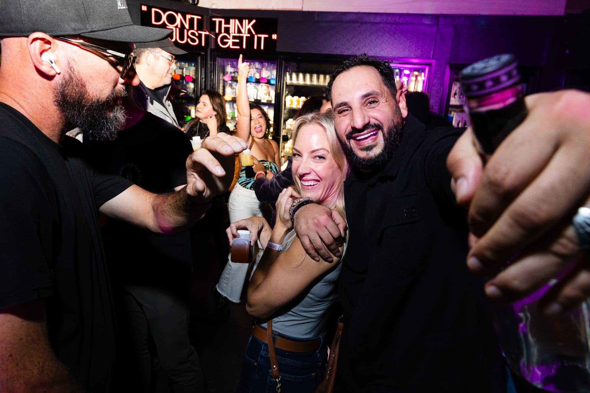 Kristen Tener hugs her friend who is holding a bottle of tequila as they both smile toward the camera. 