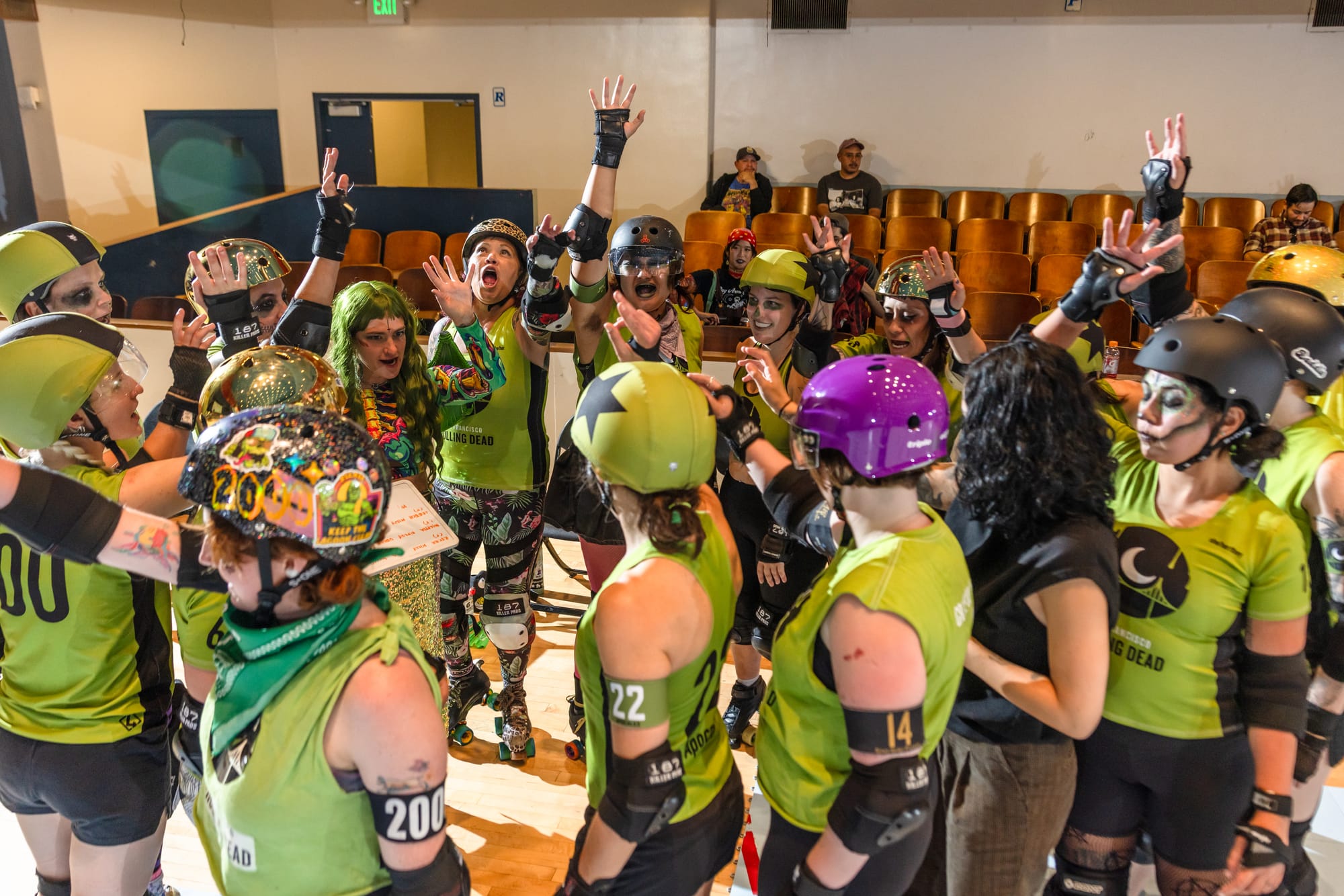 A big group of skaters all wearing green jerseys holding up their hands and shouting in unison.