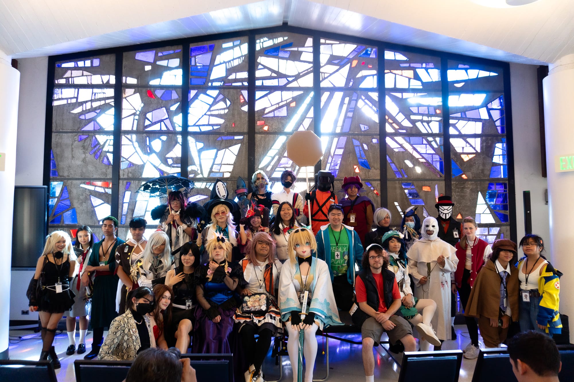 A crowd of people dressed as anime and video game characters pose in front of a large stained glass window.