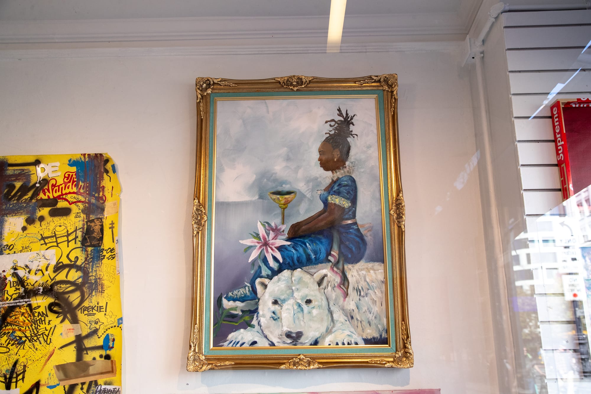 A large ornate oil painting of a woman sitting atop a polar bear hangs in a gold frame.