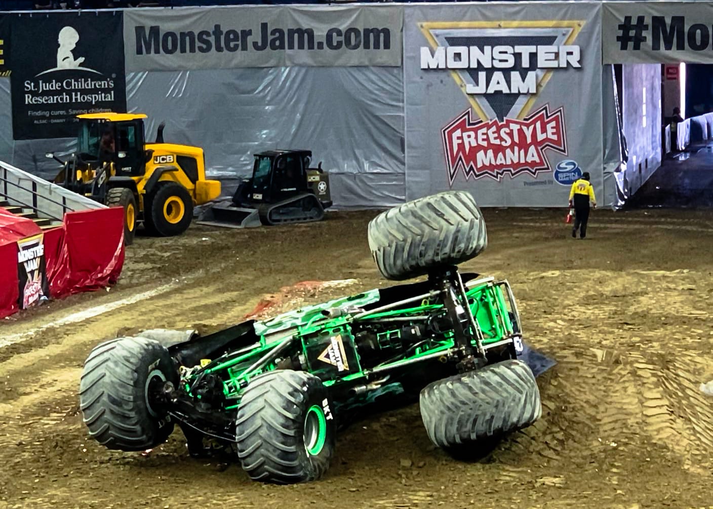 A green, upside down monster tuck lays in the dirt.