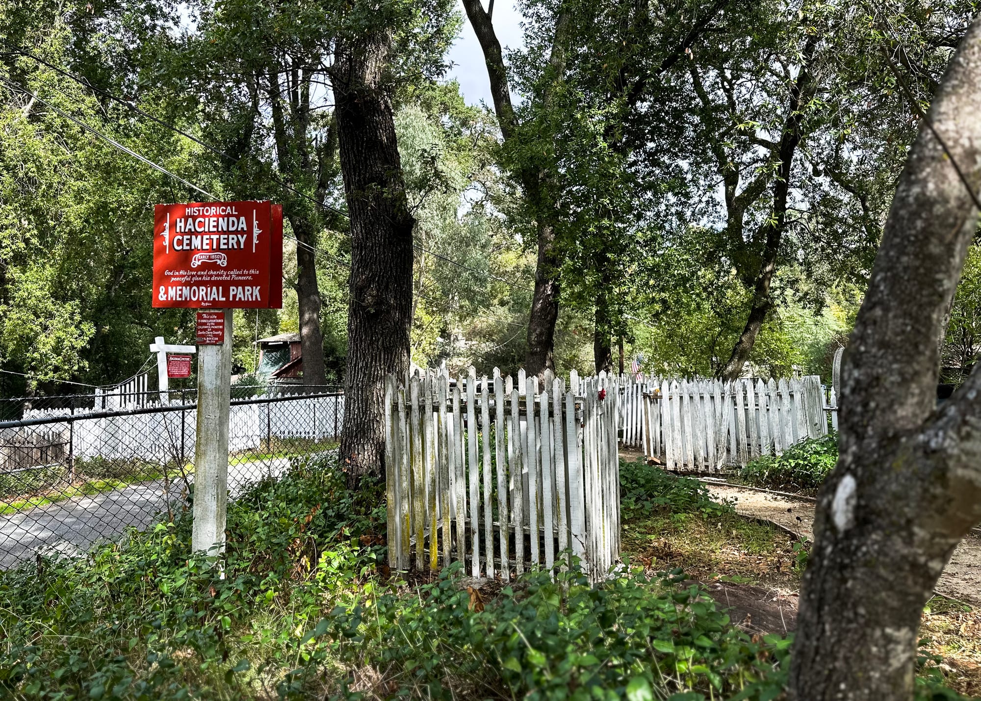 Short white fences surrounding gravesites. A red sign reads "Historical Hacienda Cemetery."