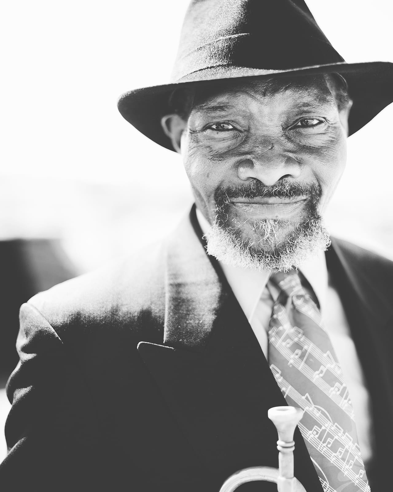 a black and white portrait of an older Black man wearing a suit and tie with musical notes on it