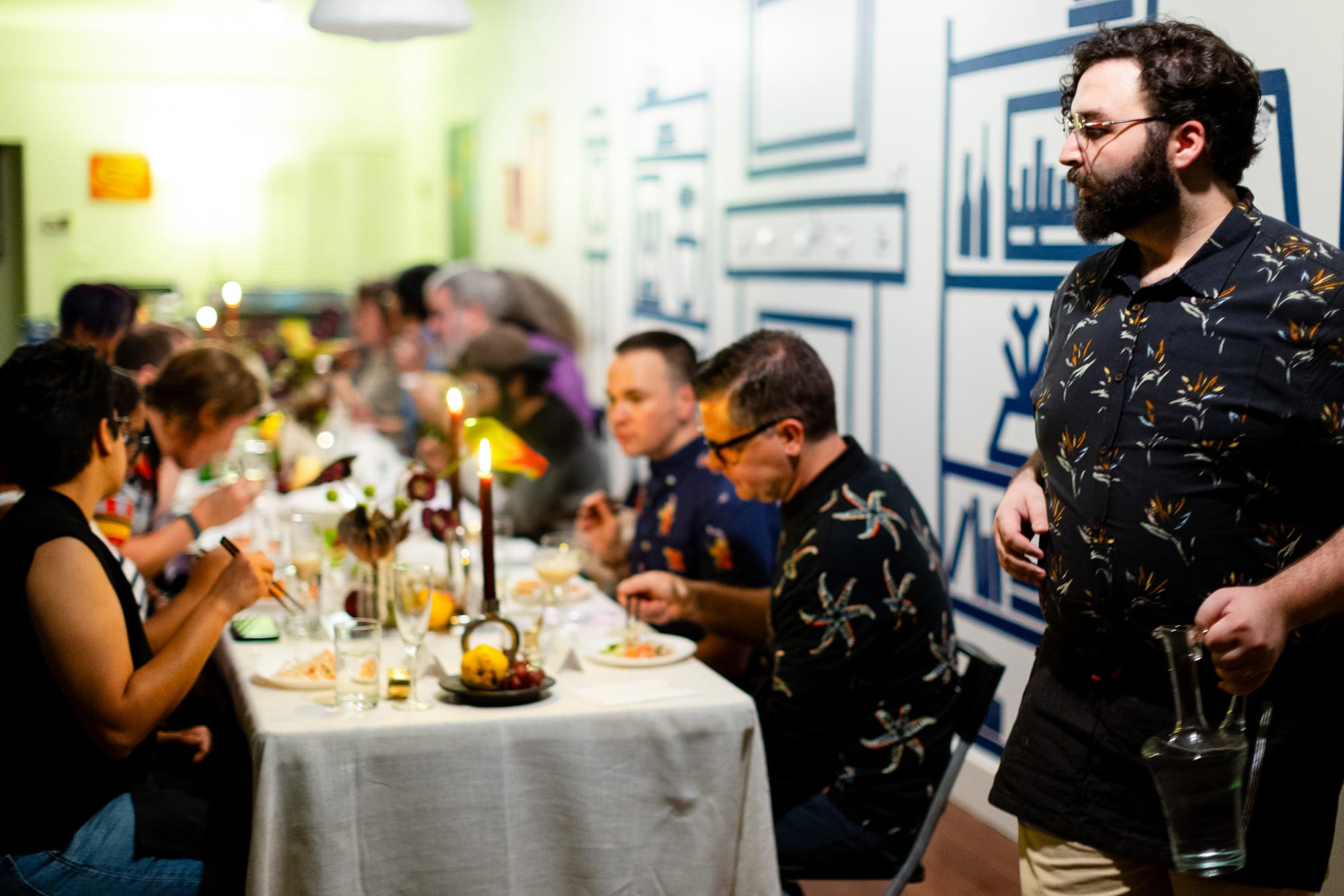 David Cox walks around a candle lit dinner table with a pitcher of water as people eat. 
