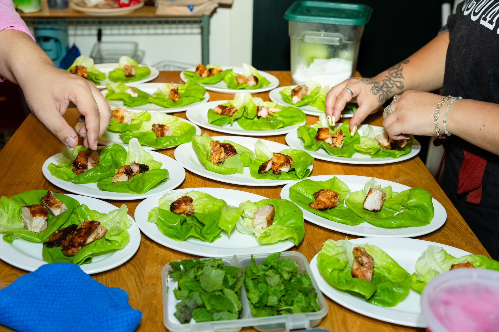 Two different sets of hands place chunks of chicken onto lettuce leaves.