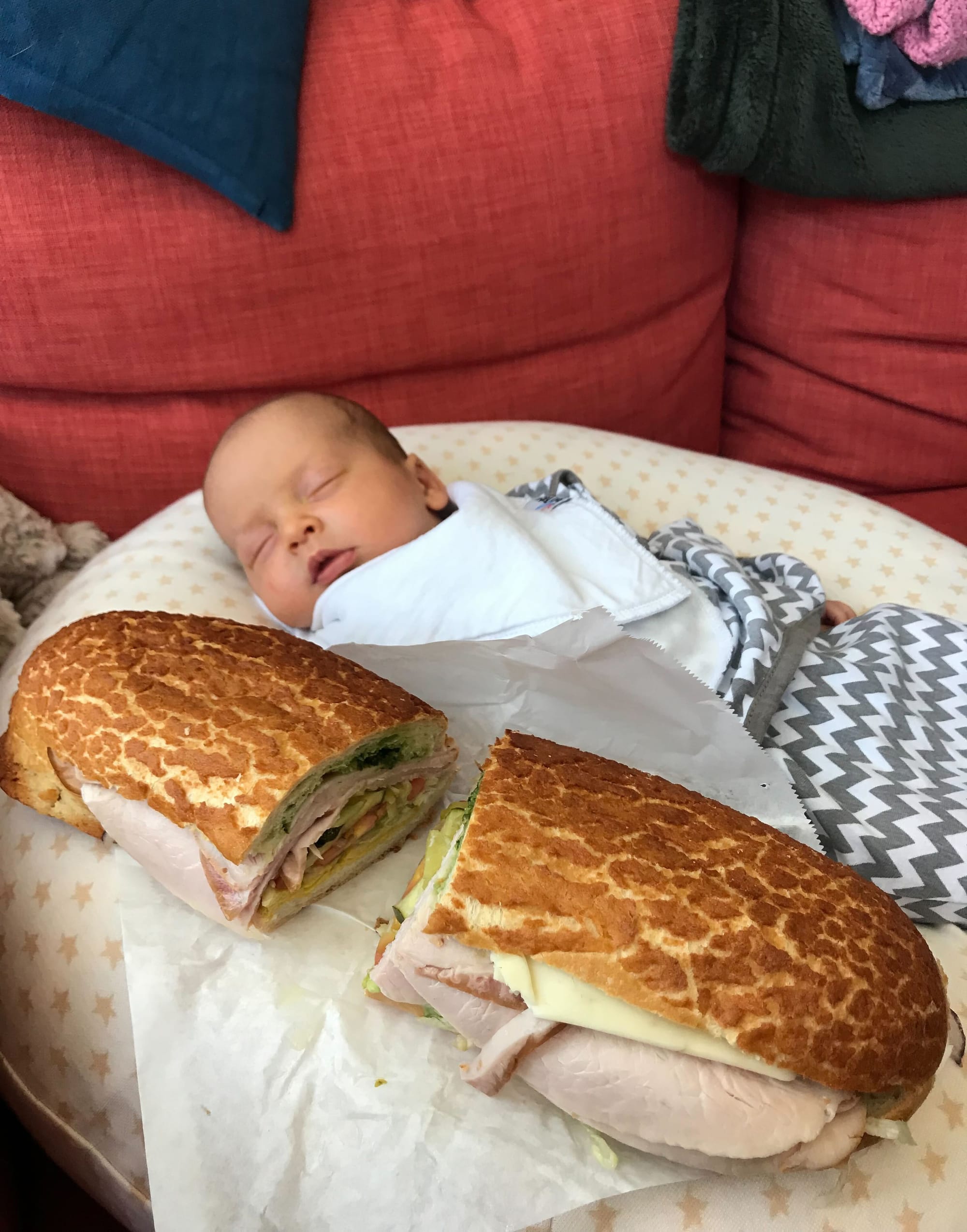 a large turkey sandwich on Dutch crunch bread next to a sleeping infant