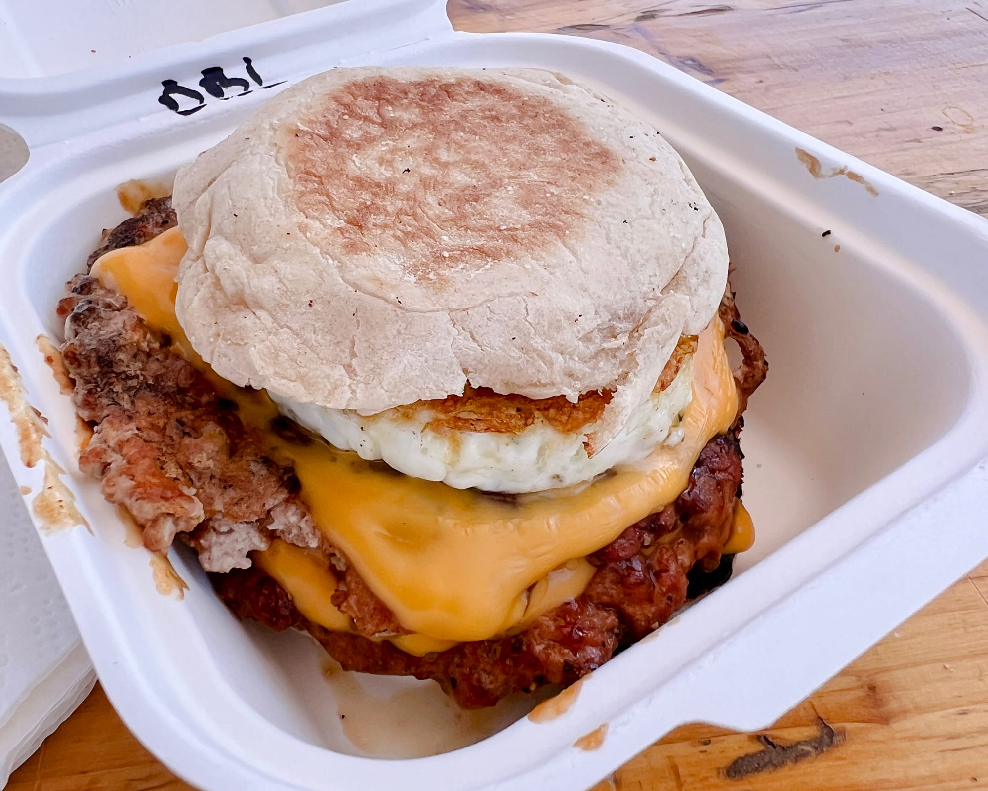 Close-up of a breakfast sandwich on an English muffin with American cheese, an egg, and two sausage patties.