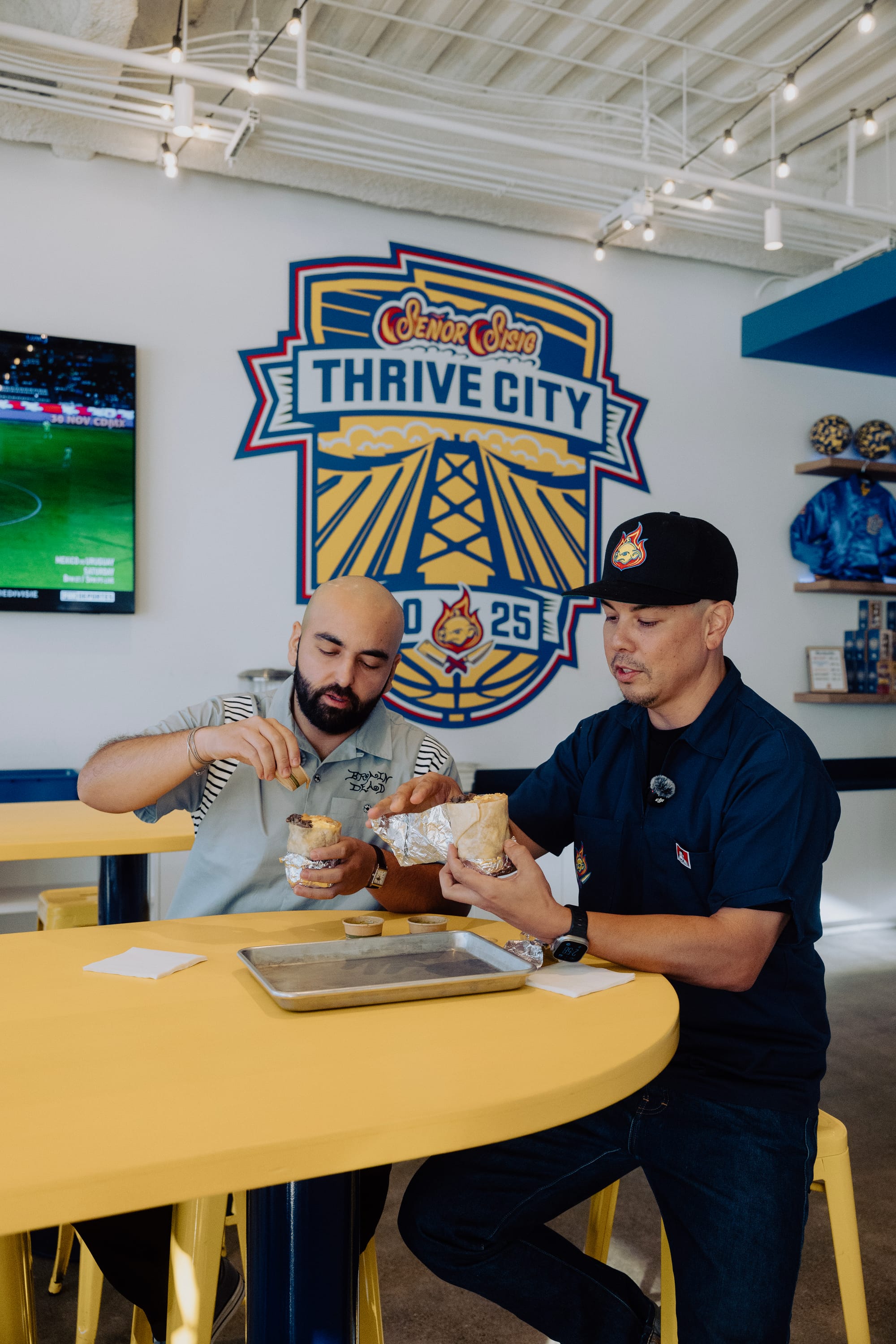 Two men sit at a yellow table and split a burrito.
