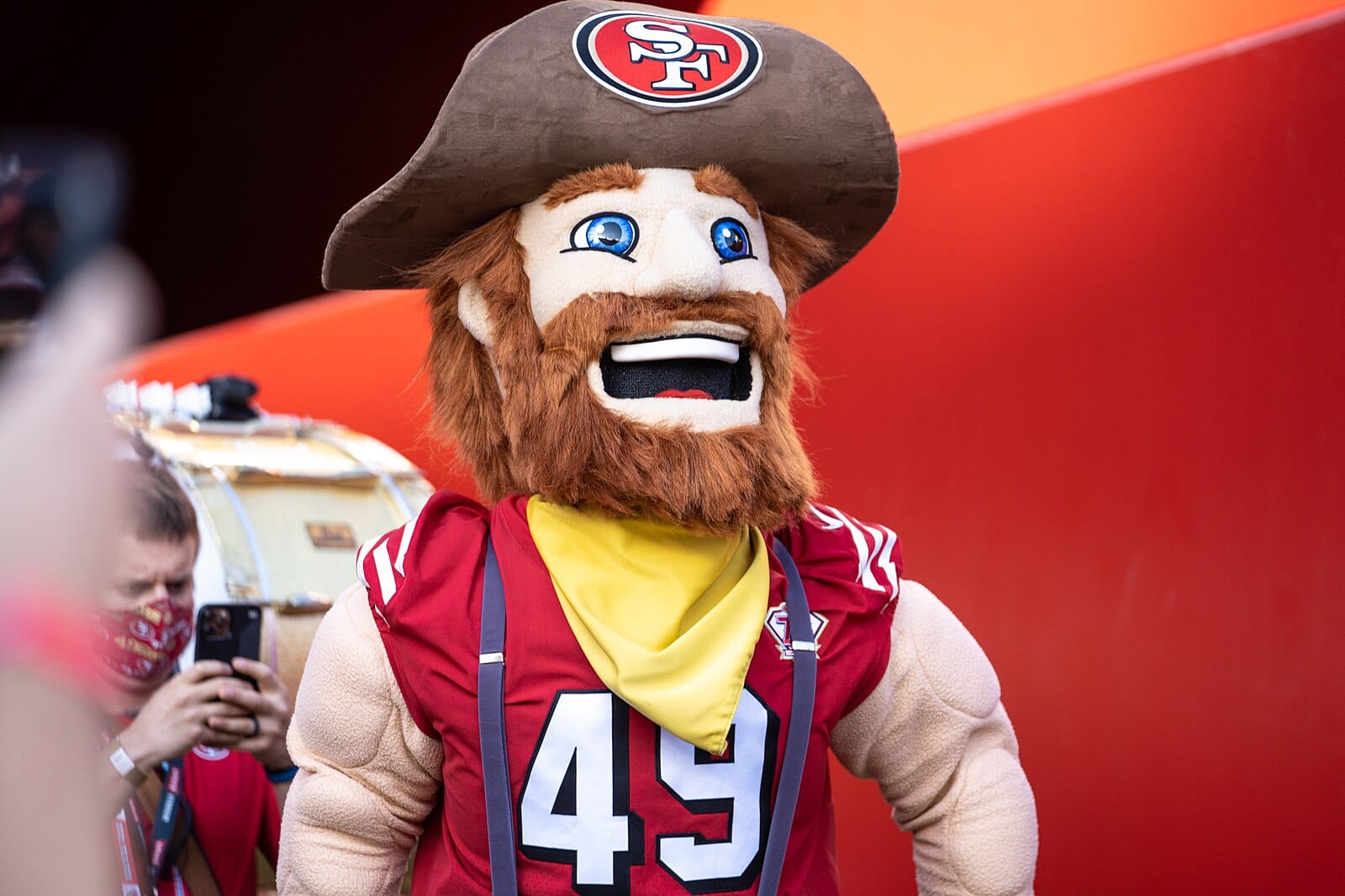 A costume that is a human man, with a big beard and blue eyes, wearing a prospectors hat and a yellow bandana. The character has big fake muscles.