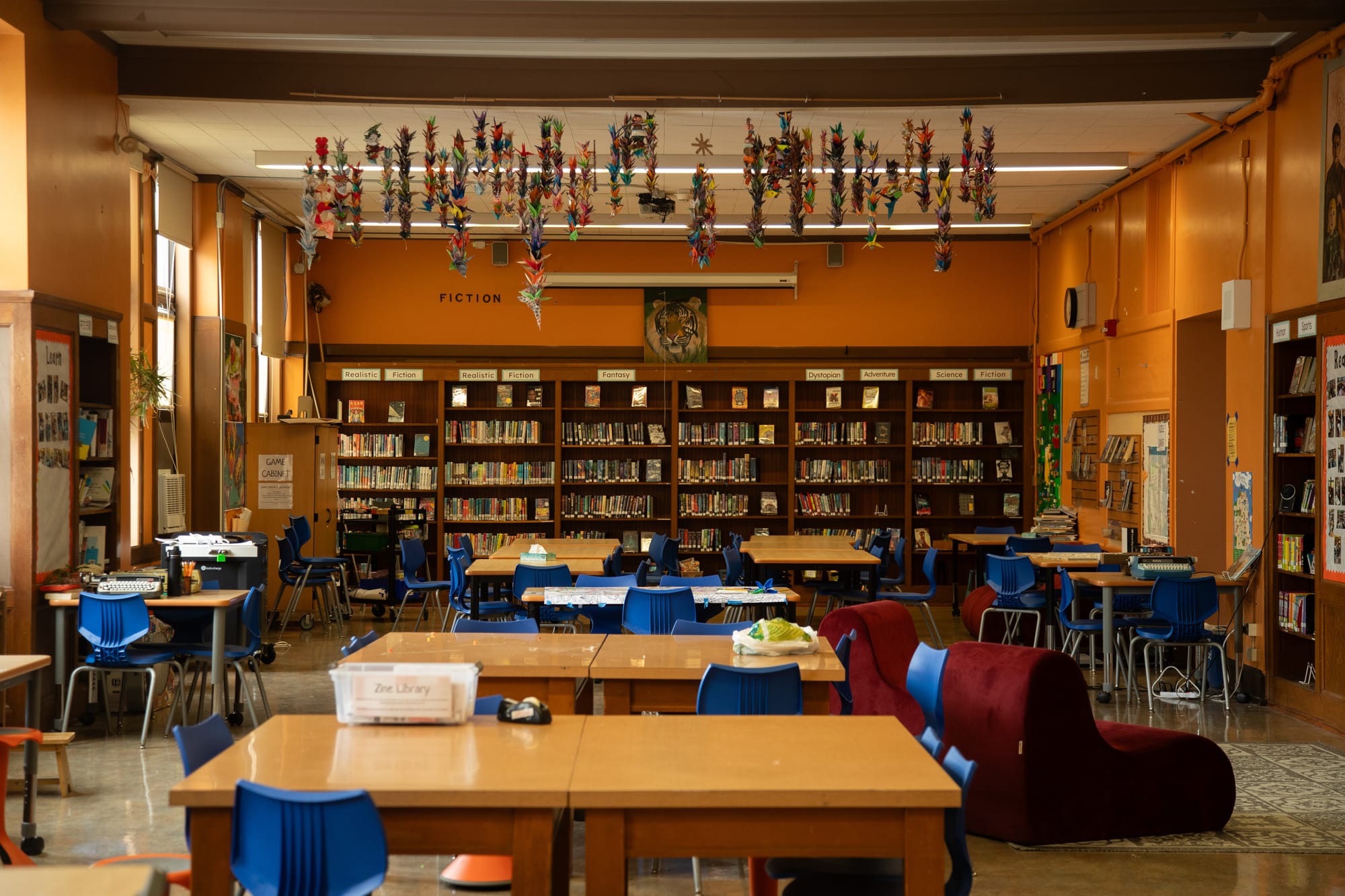 a school library with wooden tables and blue plastic chairs