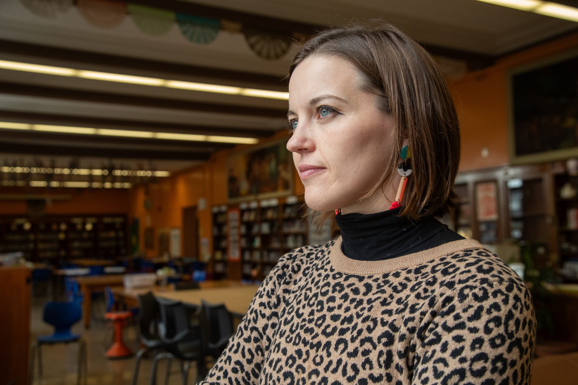 a young white woman in a leopard print sweater stands in a school library