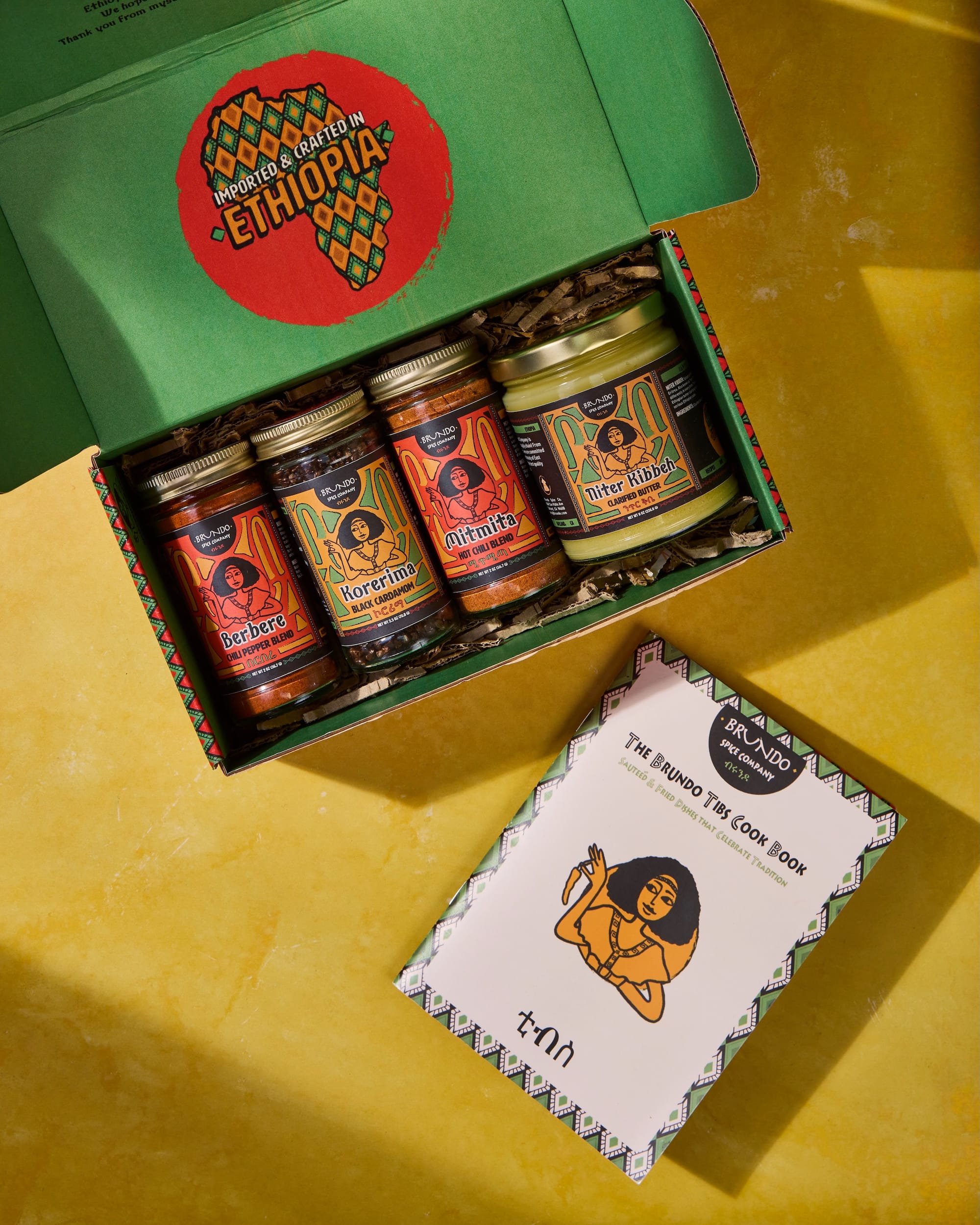 an open box of four bottles of spices, the box says 'imported & crafted in Ethiopia,' next to a cookbook called the Brundo Tibs Cook Book
