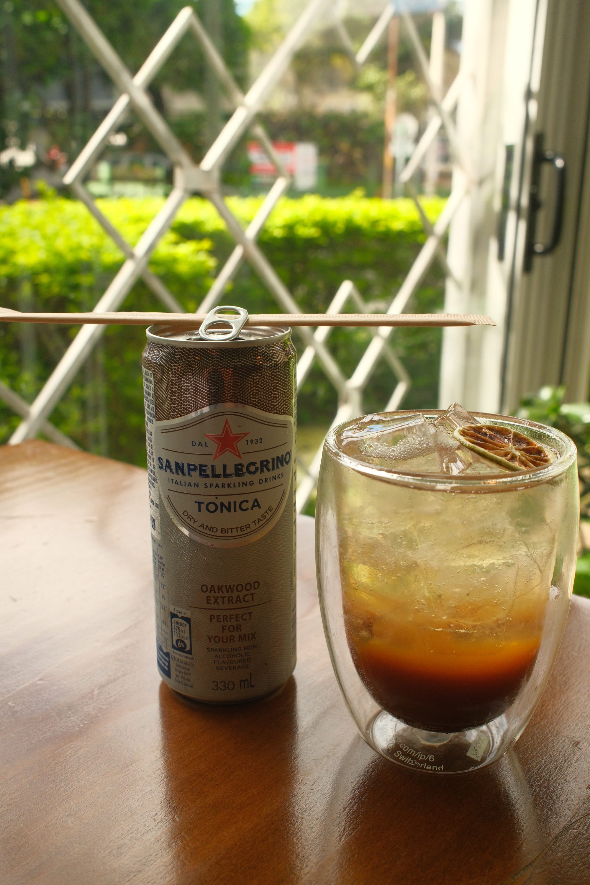 a tamarind tonic in a glass with a dried orange slice on top, with the small can next to it on a table