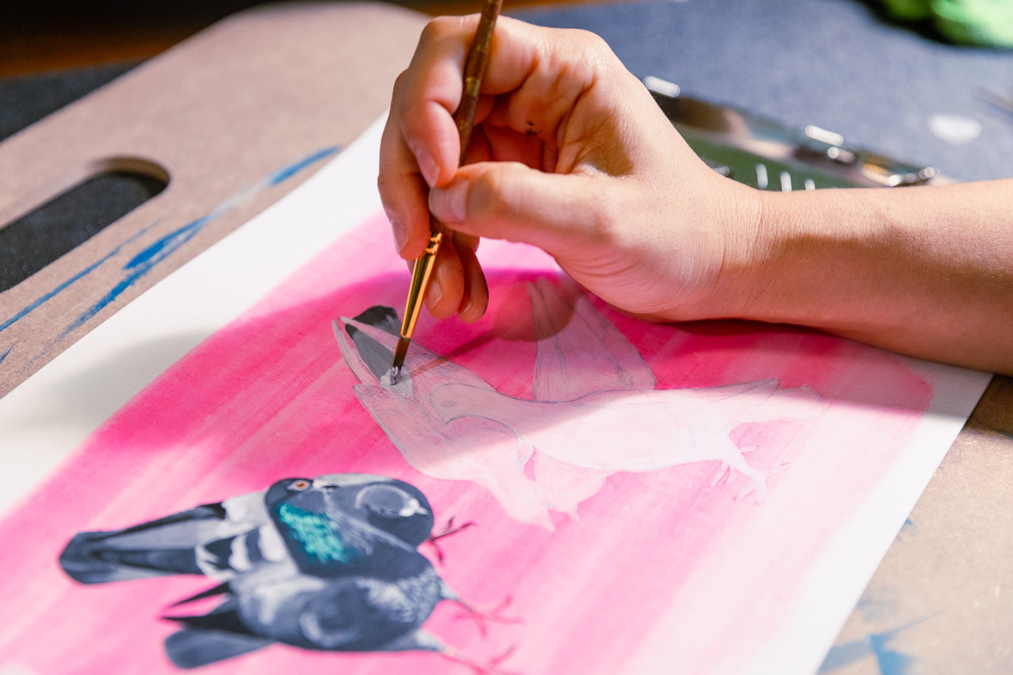 A hand holding a brush, in the process of working on a painting of a set of pigeons. 