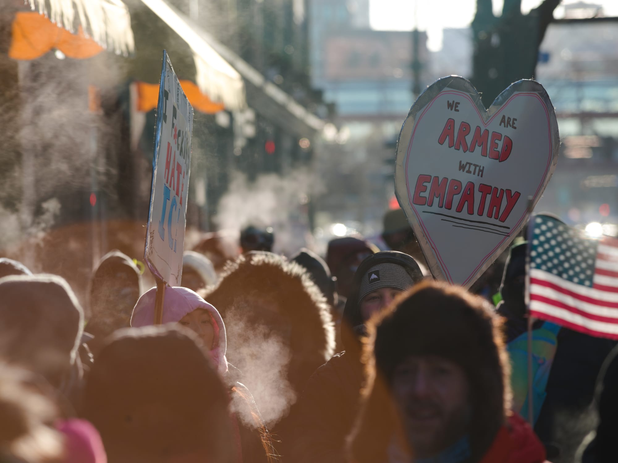 Protestors in warm clothes hold a sign that says 'we are armed with empathy.'