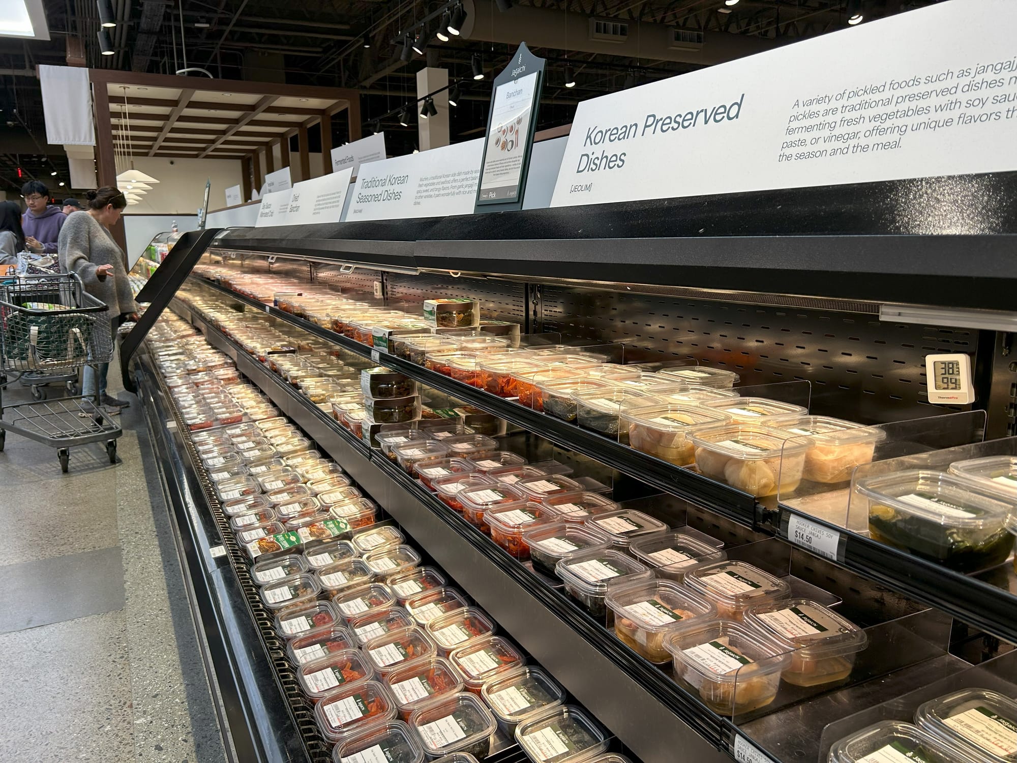 A cooler containing three shelves full of Korean side dishes and pickles. Signage above says "Korean Preserved Dishes."