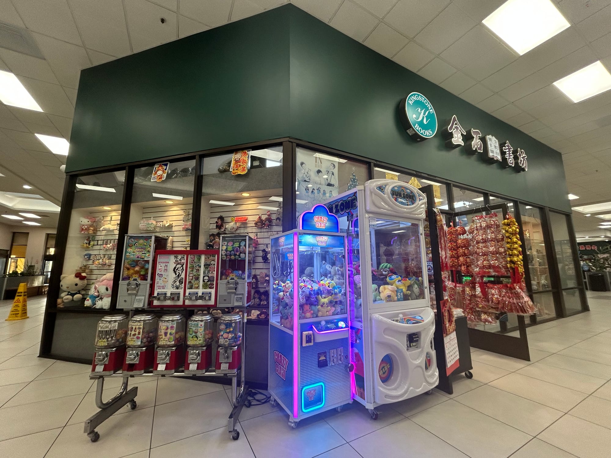 A storefront inside of a mall featuring claw machines with stuffed toys and Asian decor items.