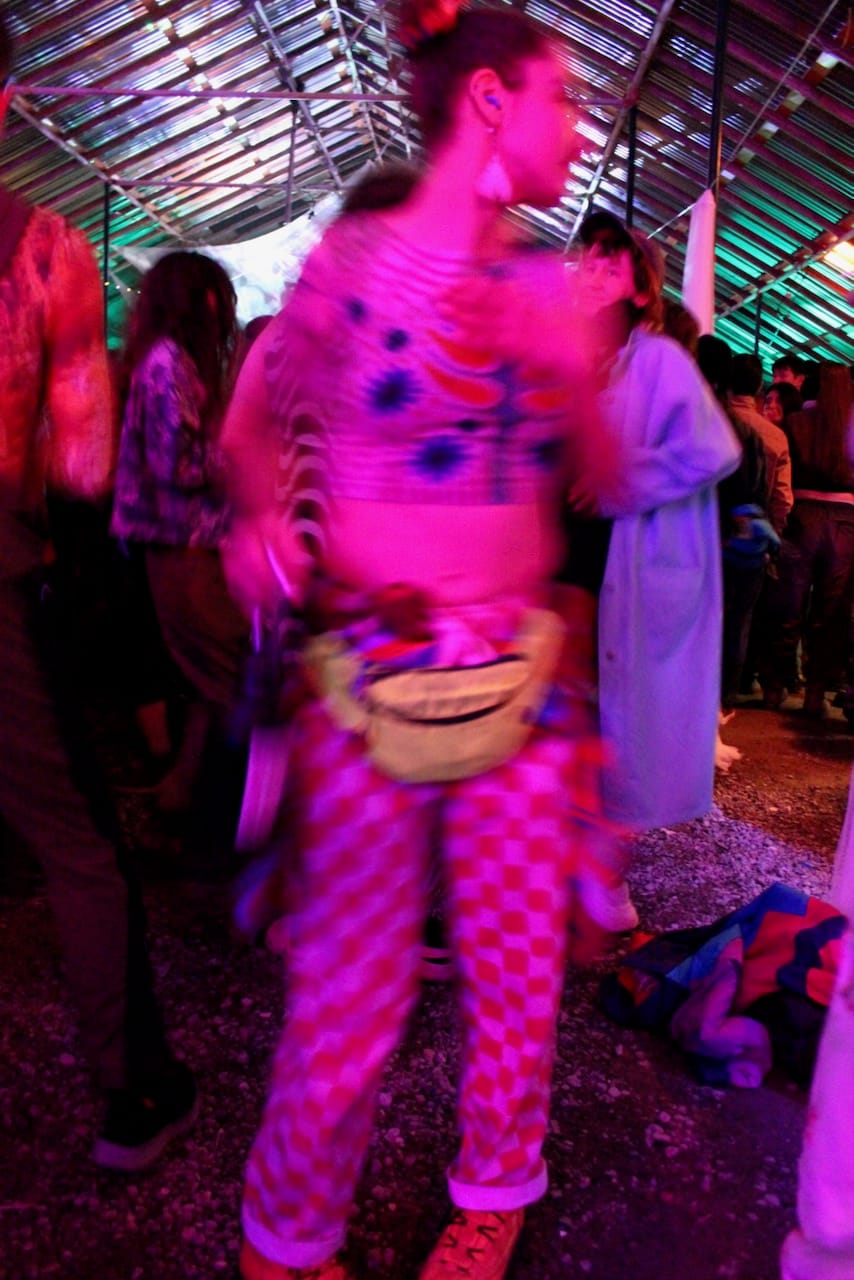 a person wearing checkered pants and a colorful top and fanny pack dances to music.