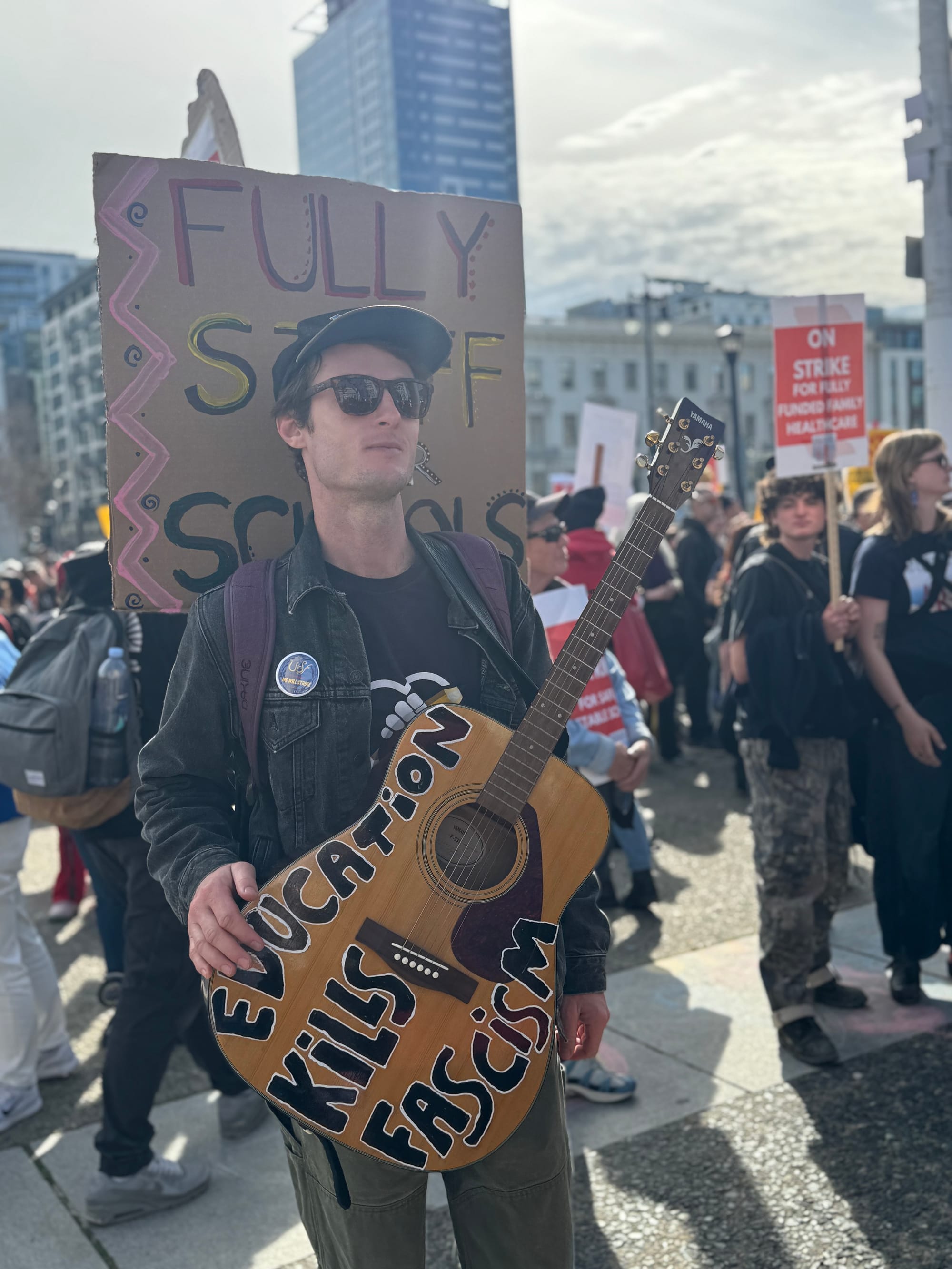 a man holds a guitar that says 'education kills fascism'