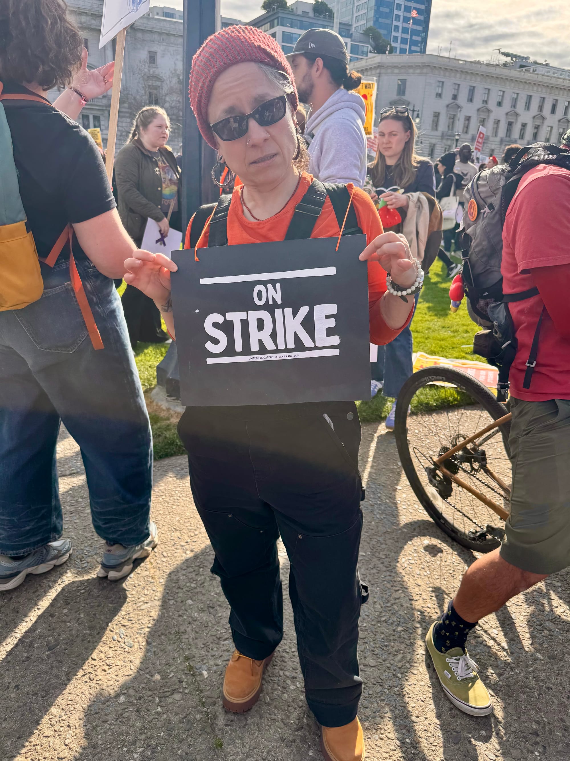 a person in black overalls holds a sign that says 'on strike'