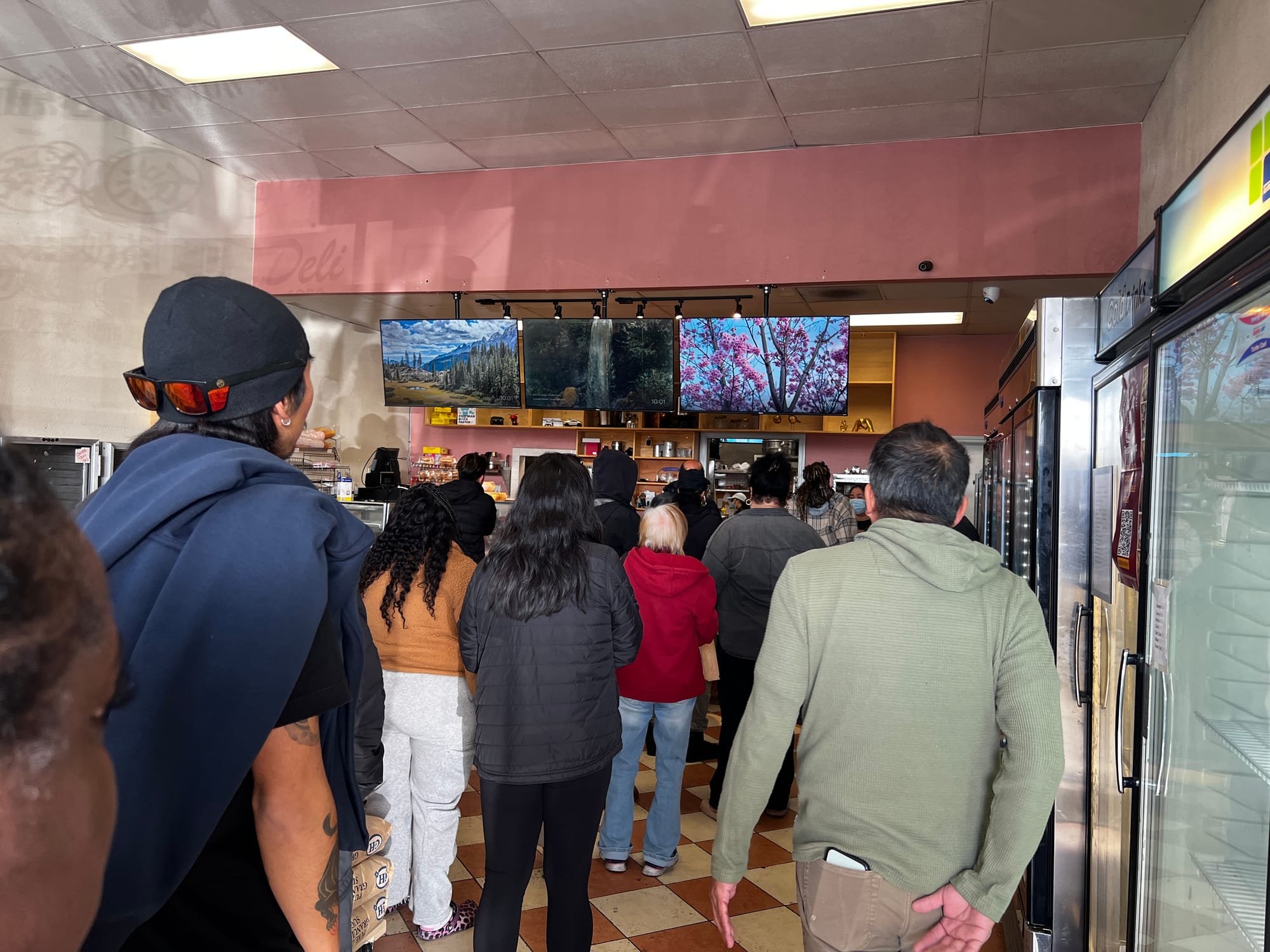 A dozen people gathering inside of a bakery, waiting their turn to order.
