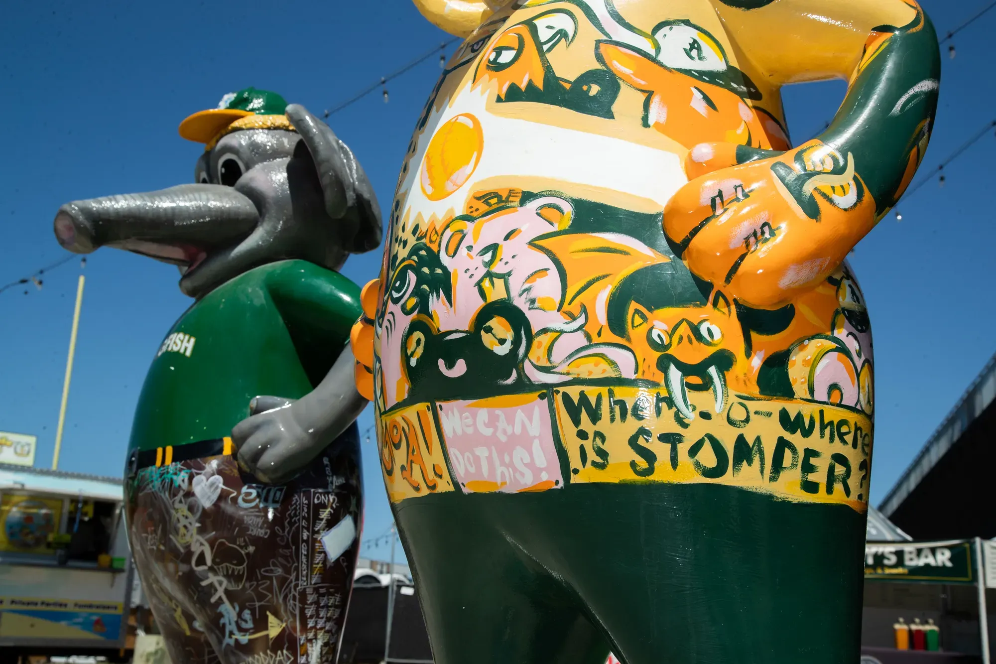 Two statues depict an anthropomorphic elephant in baseball gear. The one in the foreground is painted with cartoon animals and the text, "We can do this!" "Where-o-where is Stomper?"
