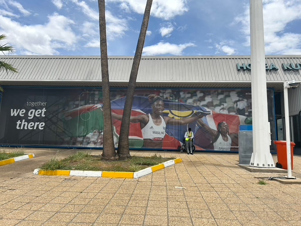 A large advertisement on the side of the Windhoek airport showing two Namibian Olympians holding their country's flag, and on the left it says "together we get there"