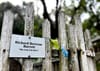 A mossy wooden fence with a small sign erected on it that says "Richard Bertram Barrett 'His Arm Lies Here'"