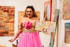 a tall beautiful Latina drag queen in a pink dress reads from a picture book in an art gallery and bookstore