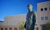 a statue of Cesar Chavez against a blue sky in front of a beige building