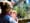 A woman and her baby in the foreground, blurry, and the background shows a bunch of shrubs and, if you look closely, a metal sculpture of dandelion puffs.
