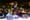 A man with dreadlocks stands on a stage in front of a crowd of people at night.